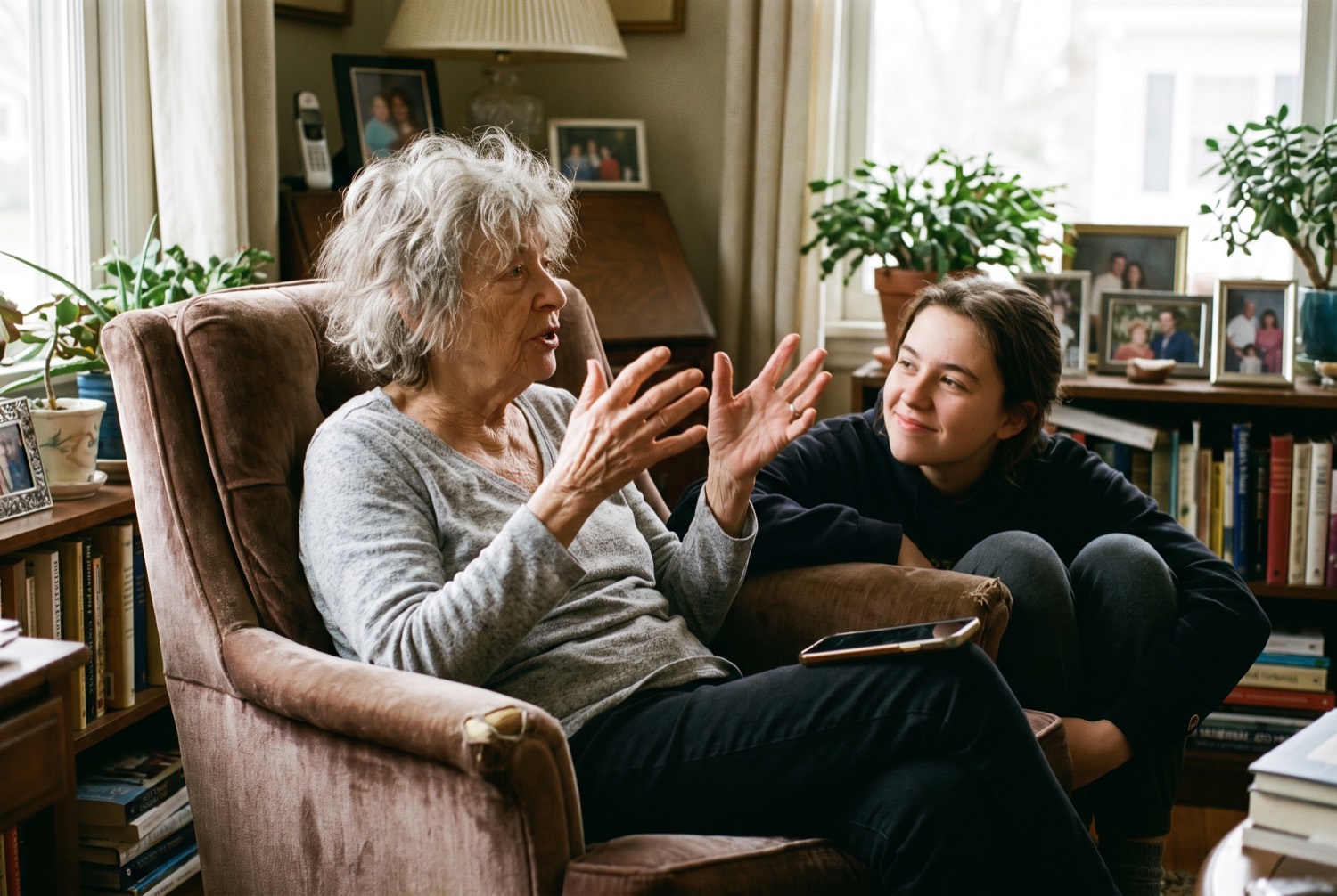 An older woman mid-sentence in an armchair, a younger person listening beside her.