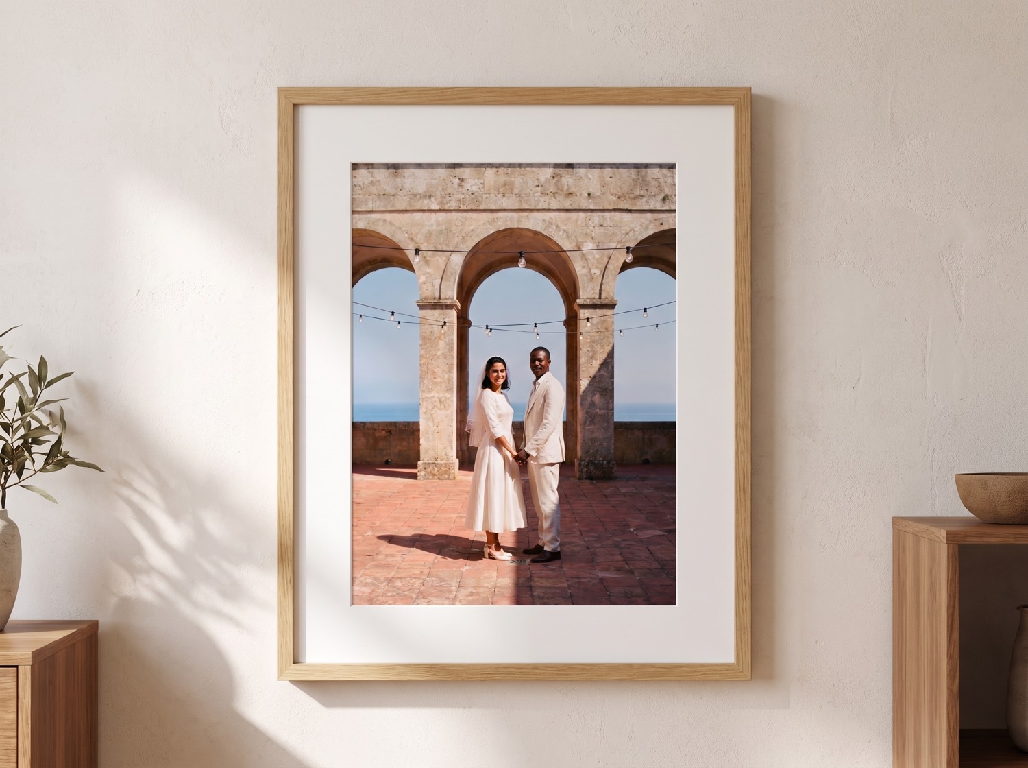 A restored family photo in a plain oak frame with a wide mount, hanging on a pale wall at home.