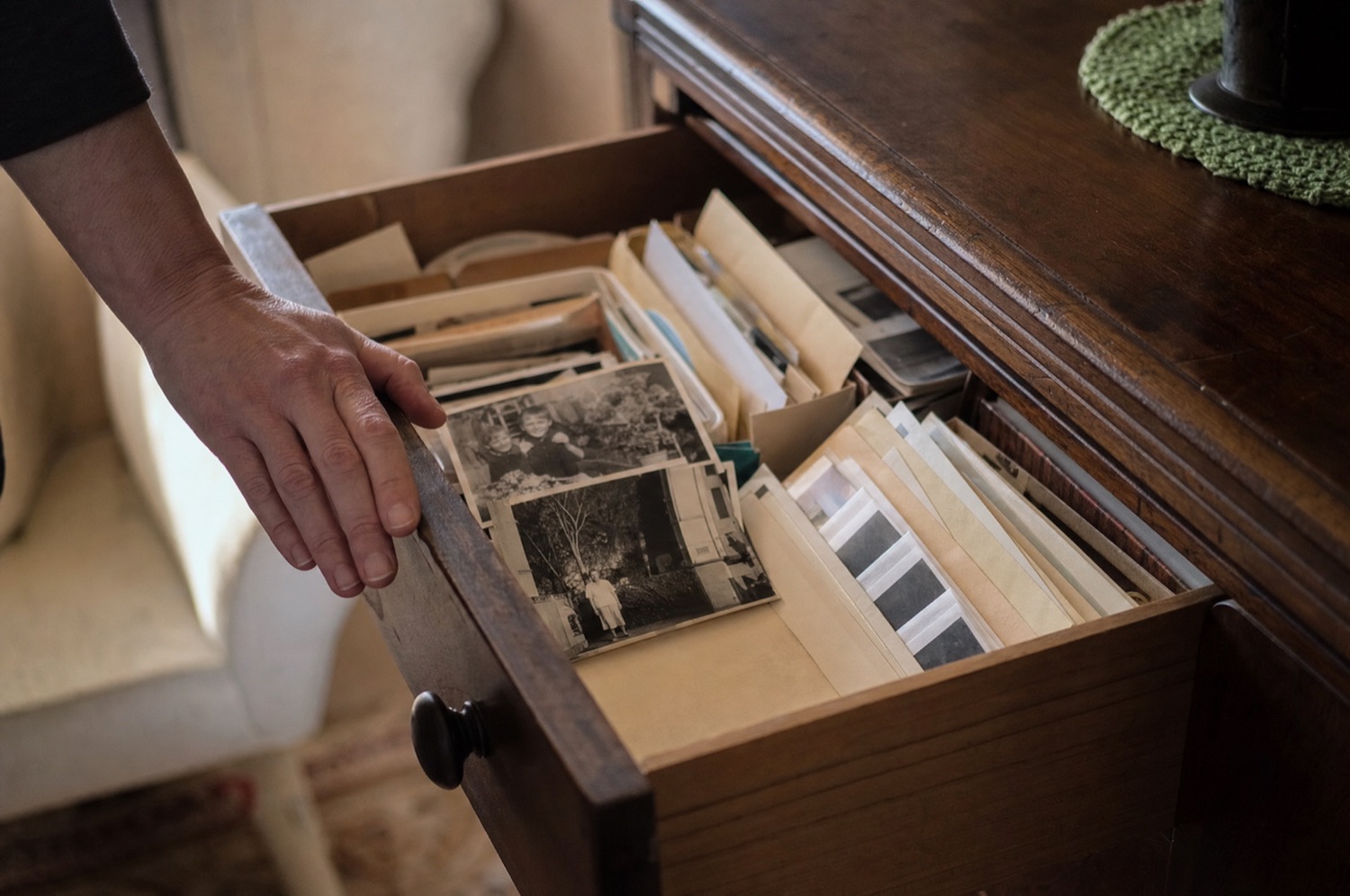 A sideboard drawer pulled open, packed with envelopes of photos, negatives in paper sleeves and loose prints.